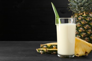 Photo of Tasty pineapple smoothie in glass and fruit on black wooden table, closeup. Space for text