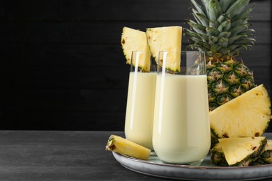 Photo of Tasty pineapple smoothie in glasses and fruit on black wooden table, closeup. Space for text