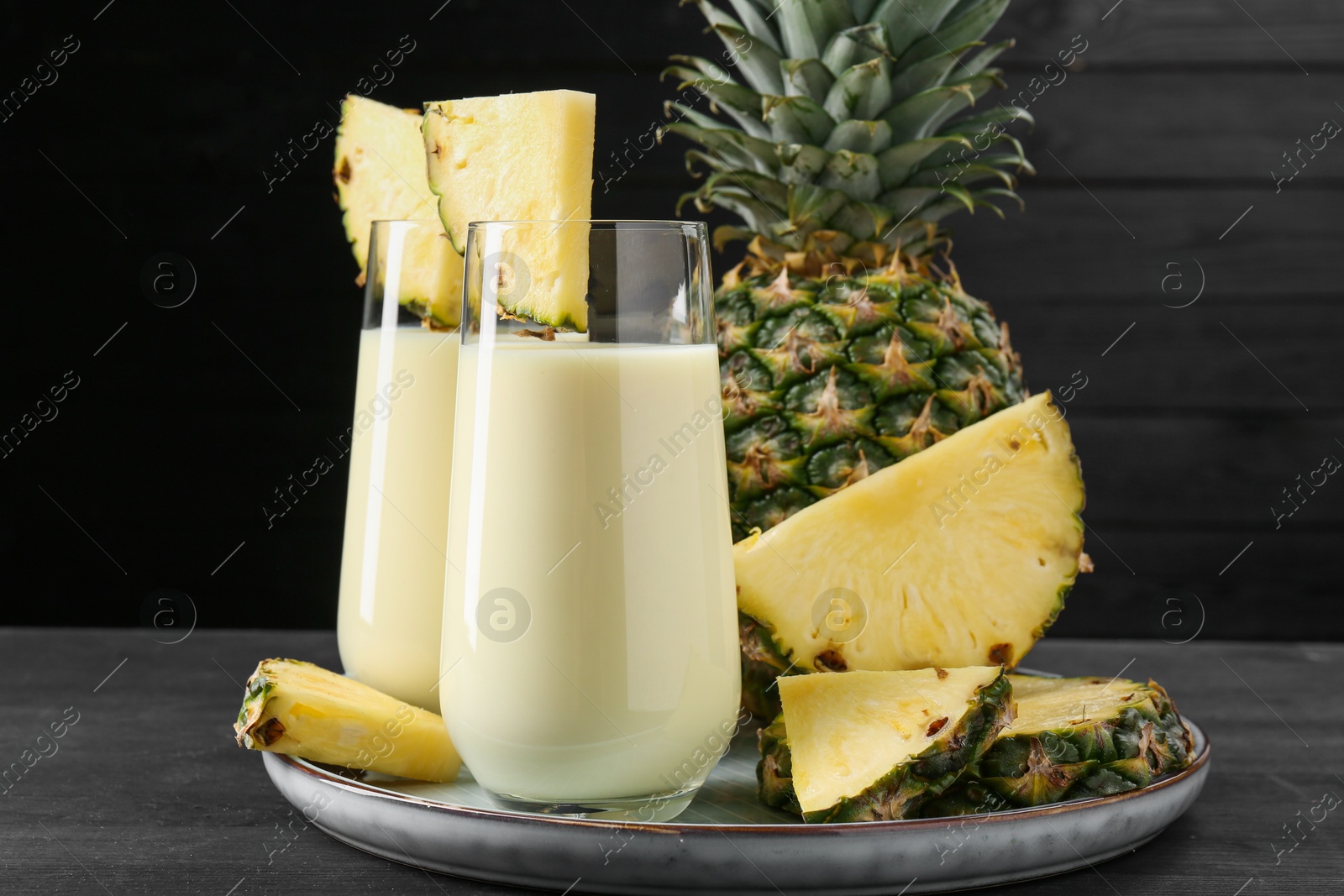 Photo of Tasty pineapple smoothie in glasses and fruit on black wooden table, closeup