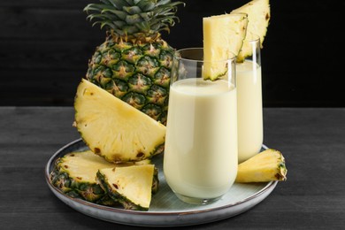 Photo of Tasty pineapple smoothie in glasses and fruit on black wooden table, closeup