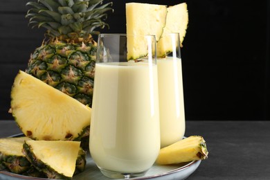 Photo of Tasty pineapple smoothie in glasses and fruit on black wooden table, closeup