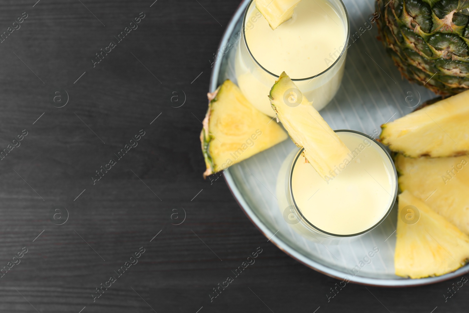 Photo of Tasty pineapple smoothie in glasses and fruit on black wooden table, top view. Space for text