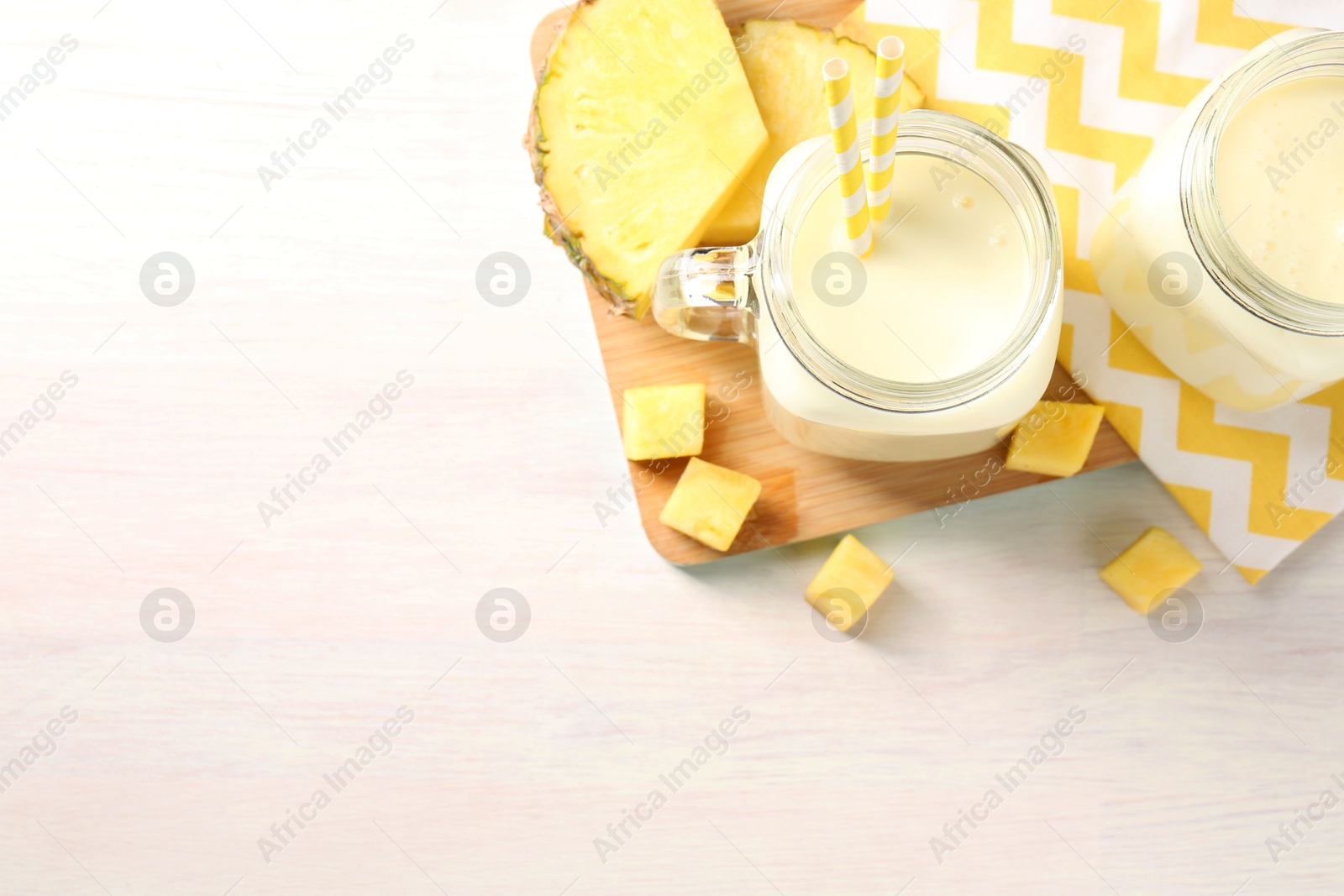 Photo of Tasty pineapple smoothie in mason jars and fresh fruit on white wooden table, top view. Space for text