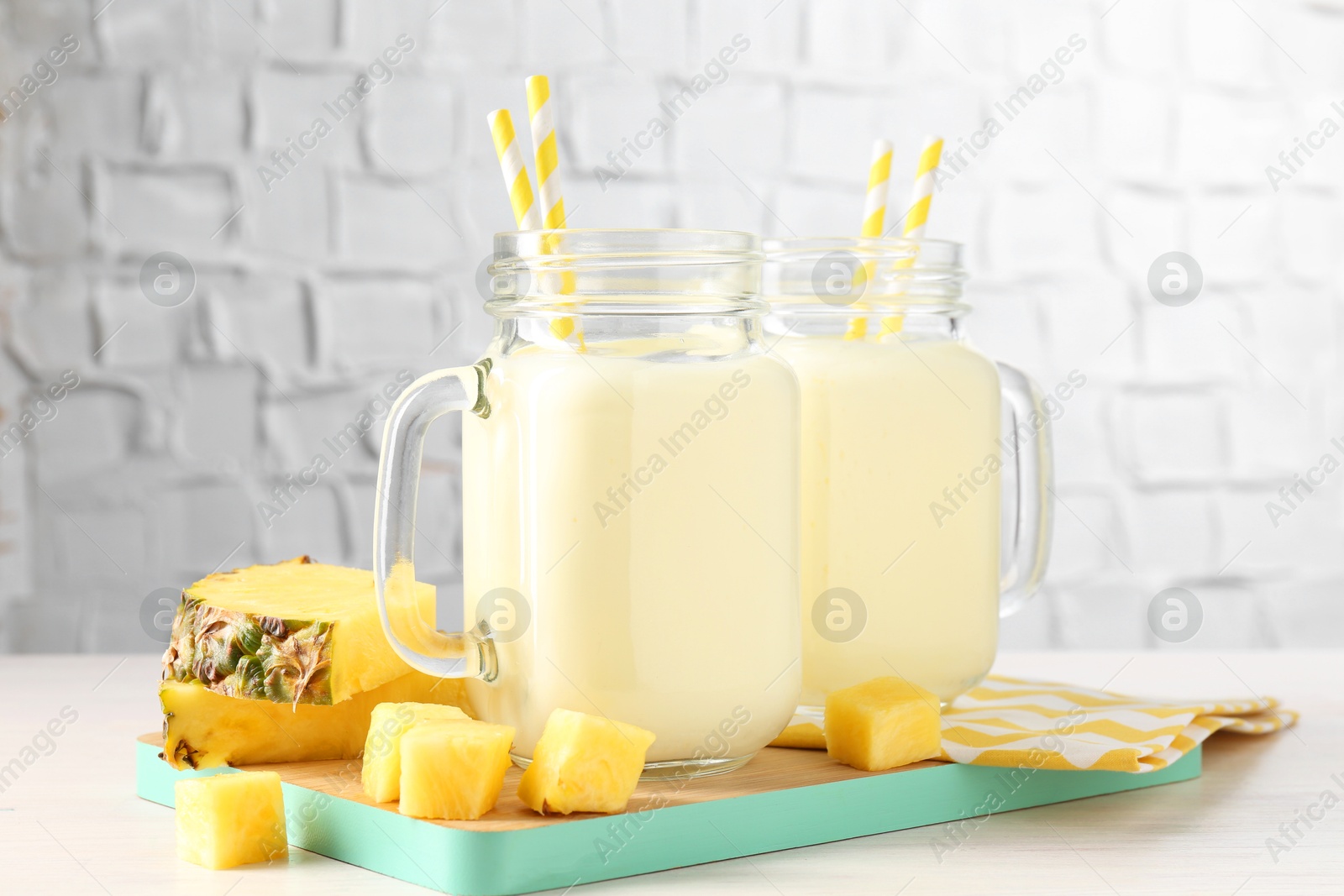 Photo of Tasty pineapple smoothie in mason jars and fresh fruit on white wooden table