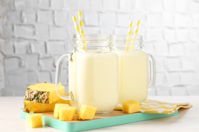 Photo of Tasty pineapple smoothie in mason jars and fresh fruit on white wooden table