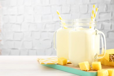 Photo of Tasty pineapple smoothie in mason jars and fresh fruit on white wooden table, space for text