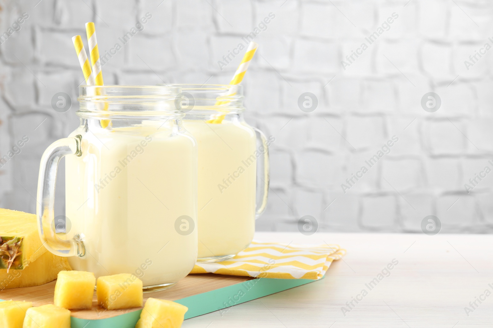 Photo of Tasty pineapple smoothie in mason jars and fresh fruit on white wooden table, space for text