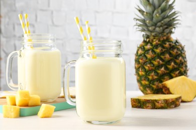 Photo of Tasty pineapple smoothie in mason jars and fresh fruits on white wooden table