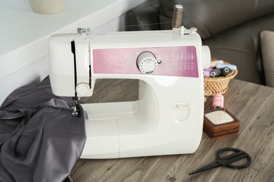 Photo of Sewing machine, gray fabric and craft accessories on wooden table indoors