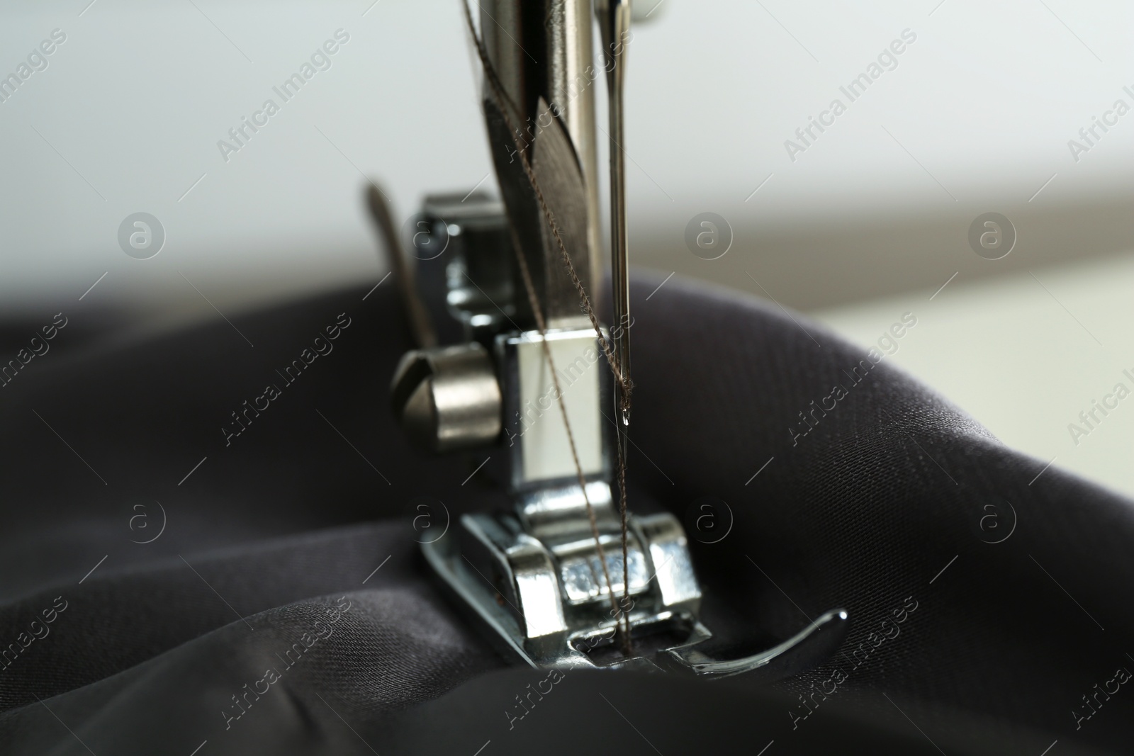 Photo of Sewing machine with gray fabric on light background, closeup