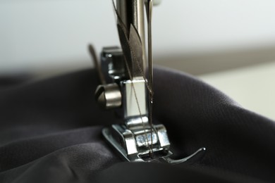 Photo of Sewing machine with gray fabric on light background, closeup