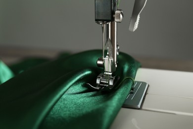 Photo of Sewing machine with green fabric on light background, closeup