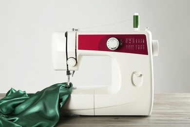 Photo of Sewing machine with green fabric on wooden table against light background