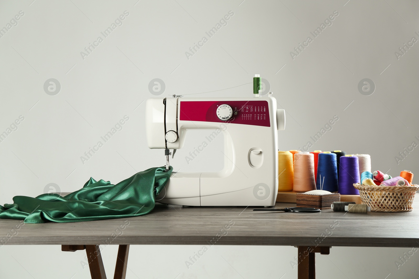 Photo of Sewing machine, green fabric and craft accessories on wooden table against light background