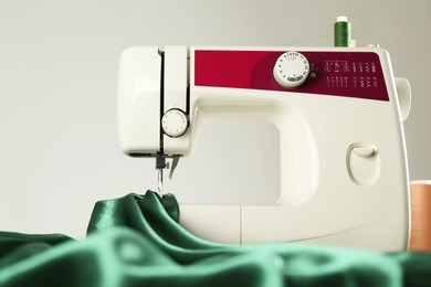 Photo of Sewing machine with green fabric on light background