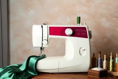 Photo of Sewing machine, green fabric and craft accessories on wooden table indoors