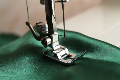 Photo of Sewing machine with green fabric on light background, closeup