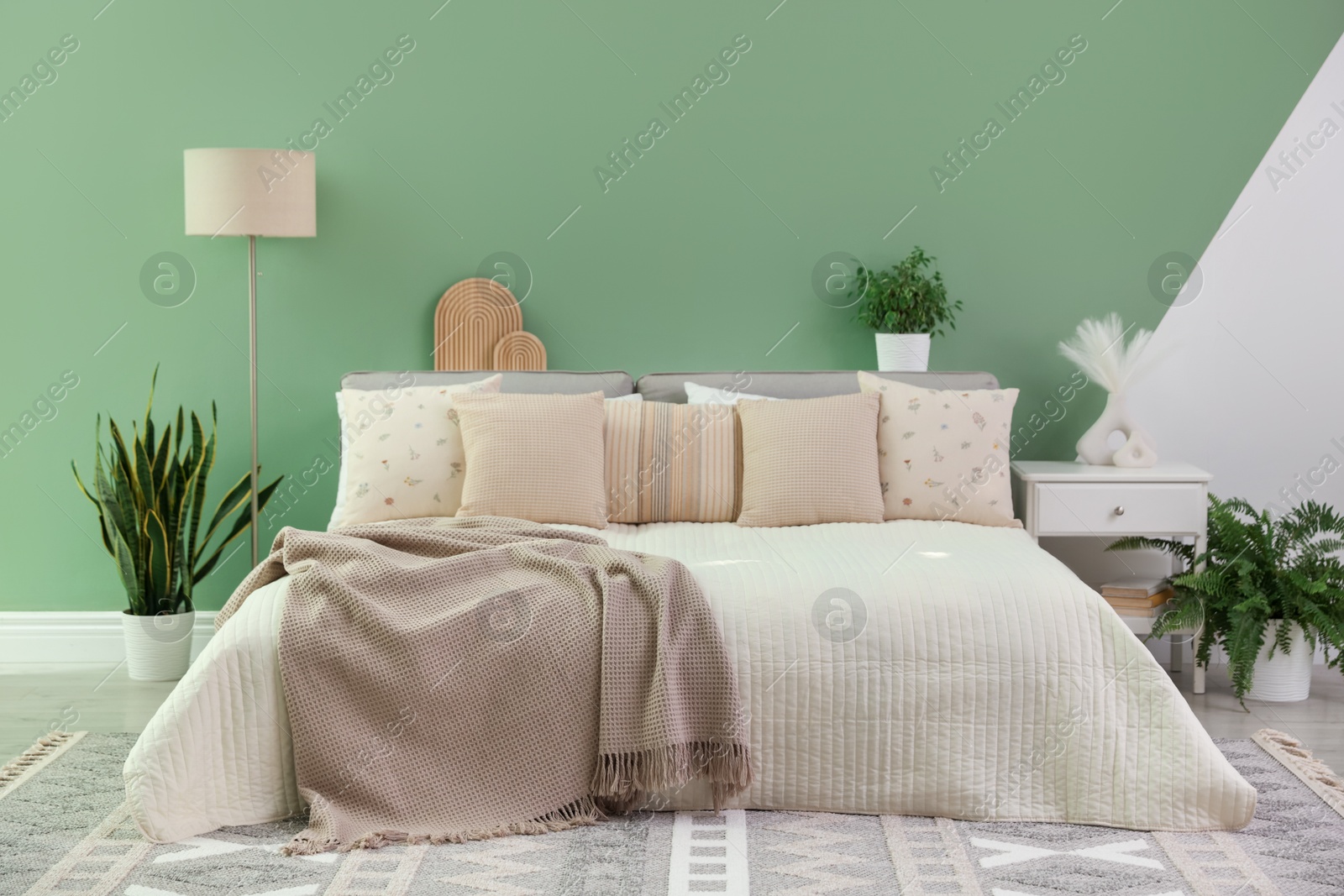 Photo of Stylish bedroom interior with large bed, houseplants and decorative elements