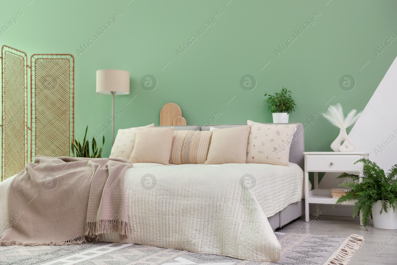 Photo of Stylish bedroom interior with large bed, houseplants and decorative elements