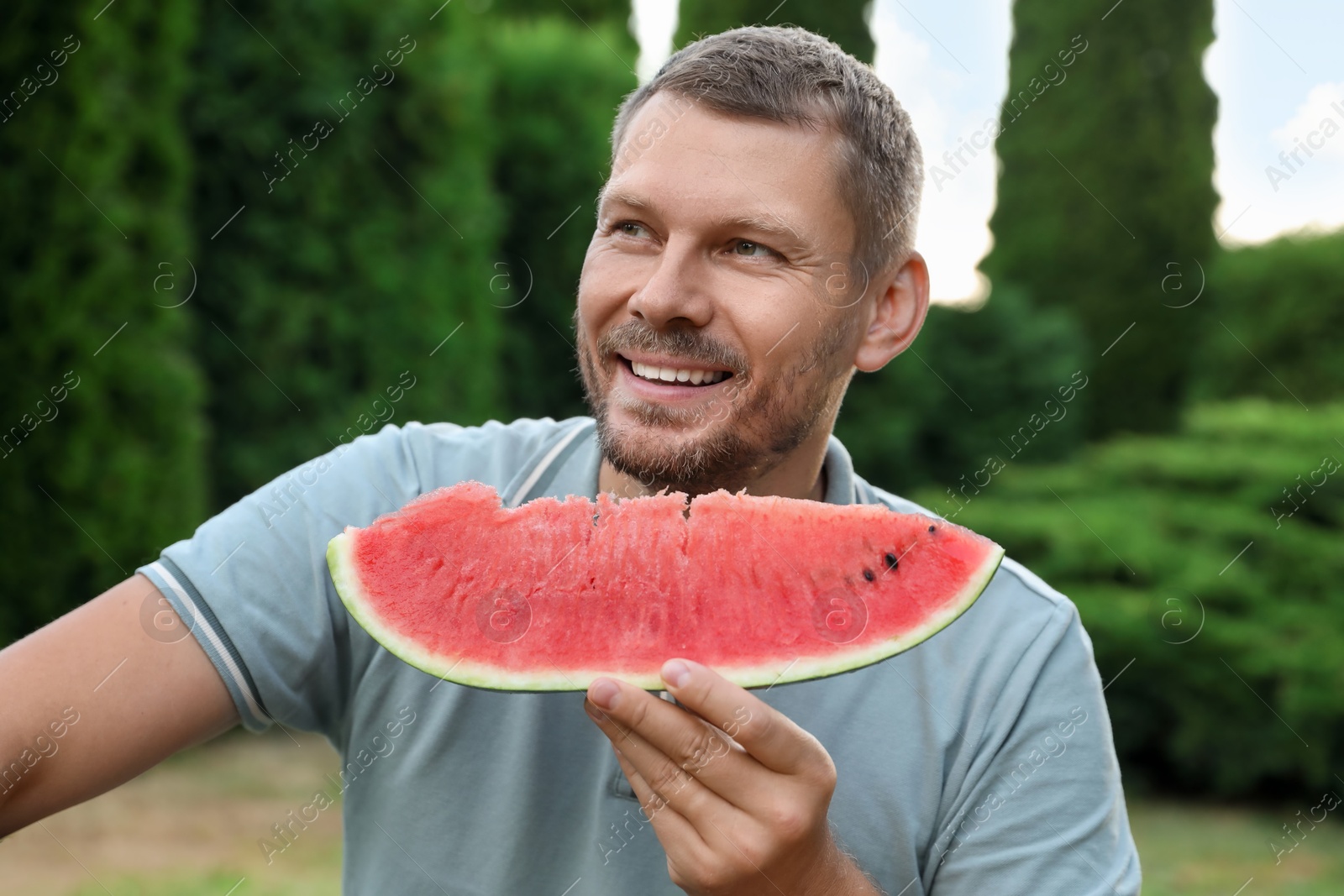 Photo of Happy man with slice of juicy watermelon outdoors