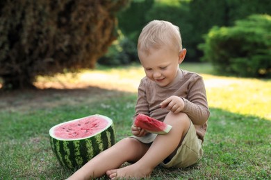 Cute little baby eating juicy watermelon on green grass outdoors