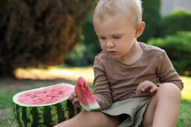 Cute little baby eating juicy watermelon on green grass outdoors