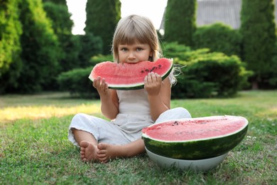 Photo of Cute little girl eating juicy watermelon on green grass outdoors