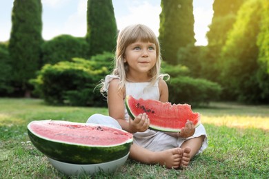 Cute little girl eating juicy watermelon on green grass outdoors