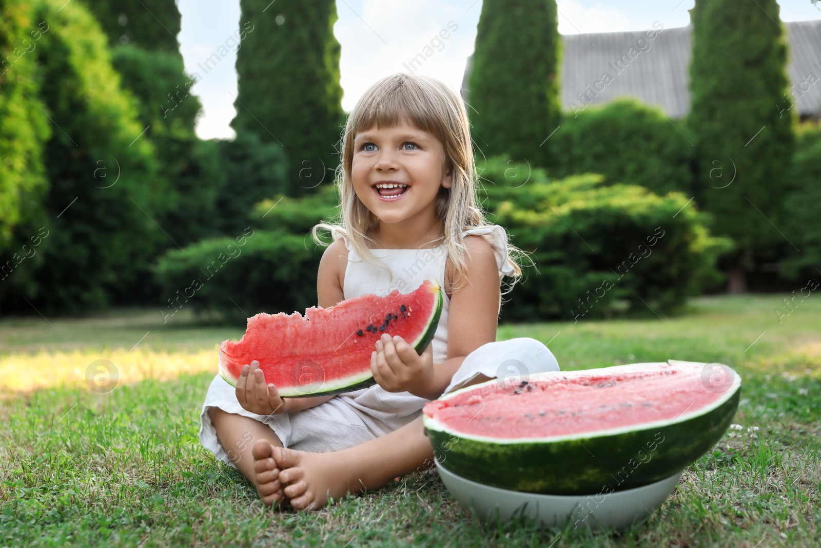 Photo of Cute little girl eating juicy watermelon on green grass outdoors