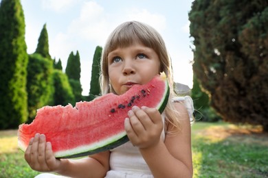 Cute little girl eating juicy watermelon on green grass outdoors