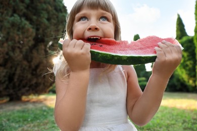 Photo of Cute little girl eating juicy watermelon on green grass outdoors