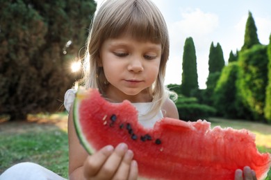 Photo of Cute little girl eating juicy watermelon on green grass outdoors