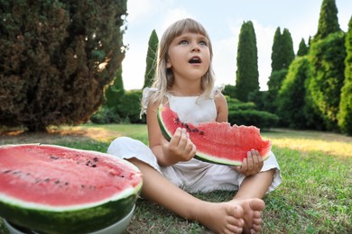 Photo of Cute little girl eating juicy watermelon on green grass outdoors