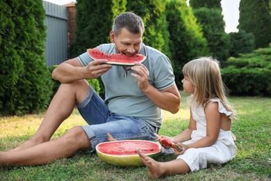 Photo of Man and his cute daughter eating juicy watermelon outdoors together