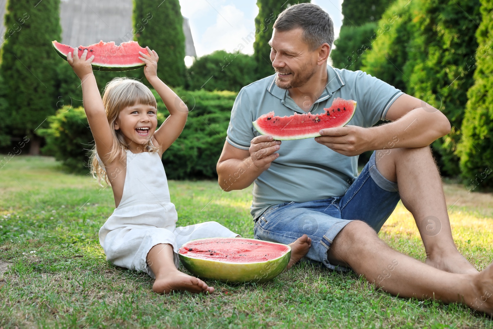 Photo of Man and his cute daughter eating juicy watermelon outdoors together