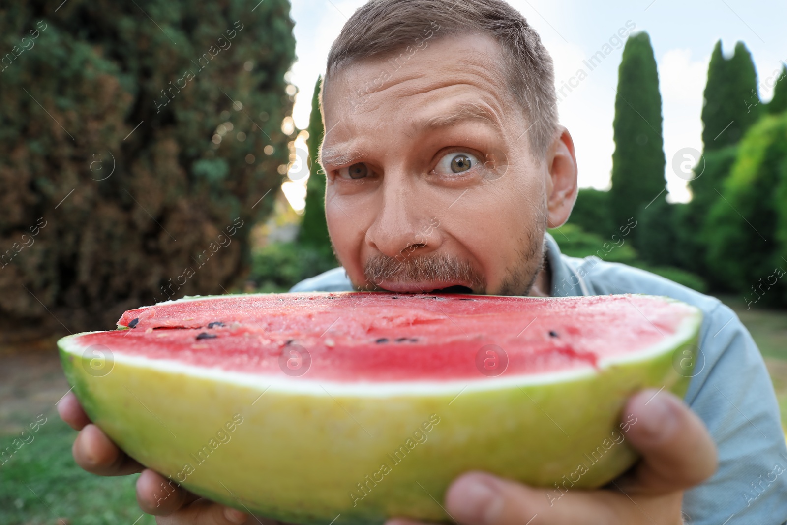 Photo of Happy man with half of juicy watermelon outdoors