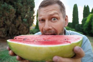 Photo of Happy man with half of juicy watermelon outdoors