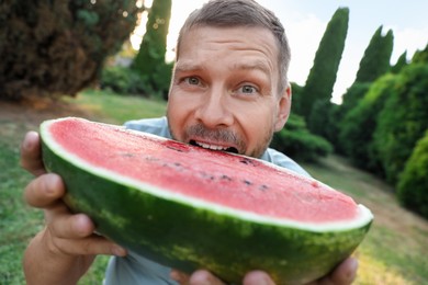 Photo of Happy man with half of juicy watermelon outdoors