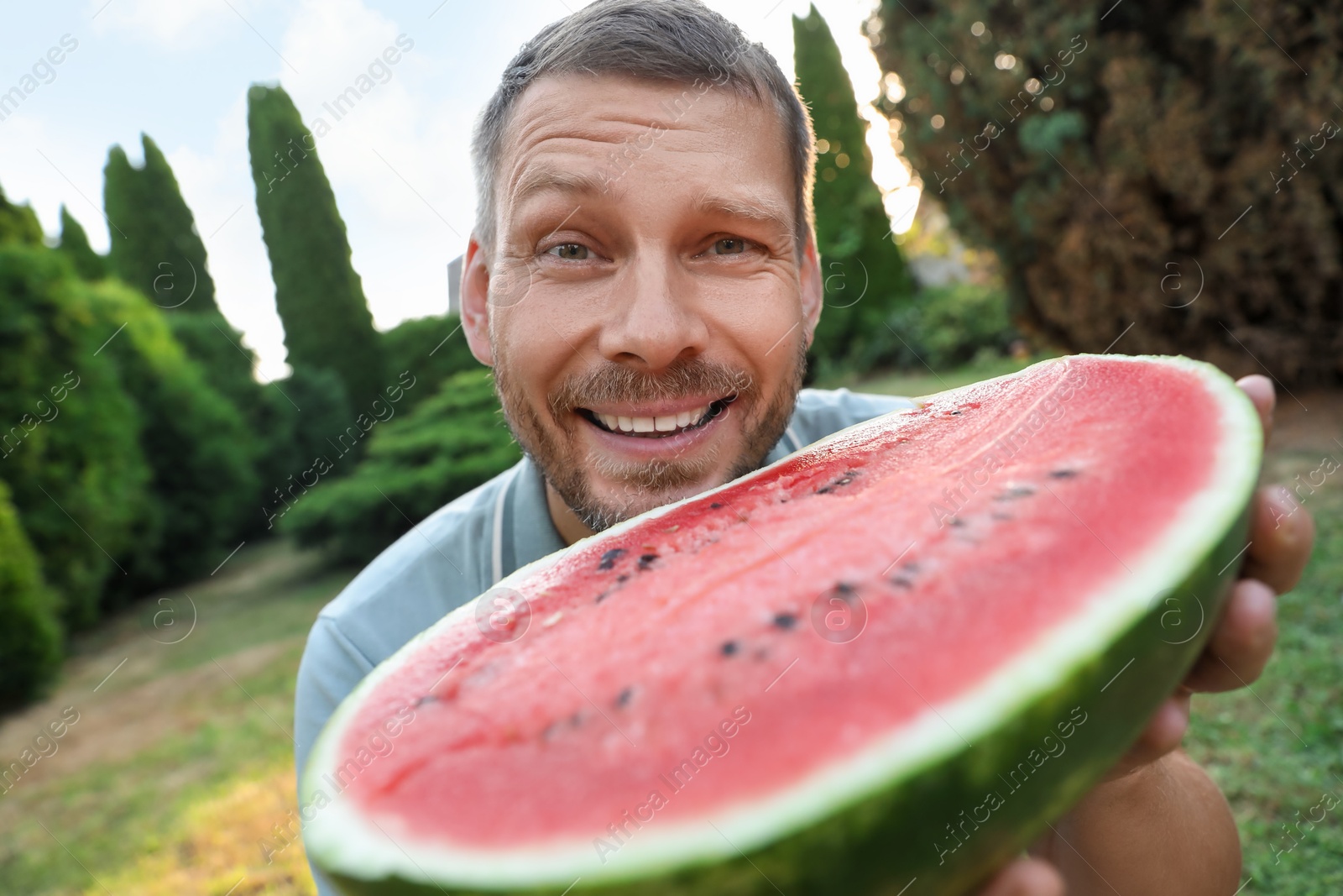 Photo of Happy man with half of juicy watermelon outdoors