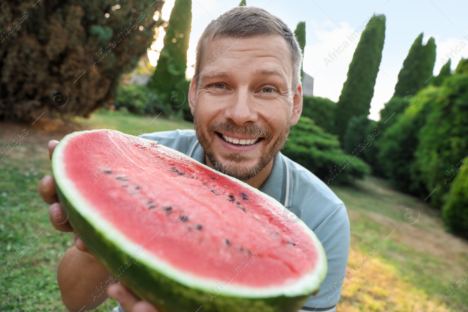 Photo of Happy man with half of juicy watermelon outdoors