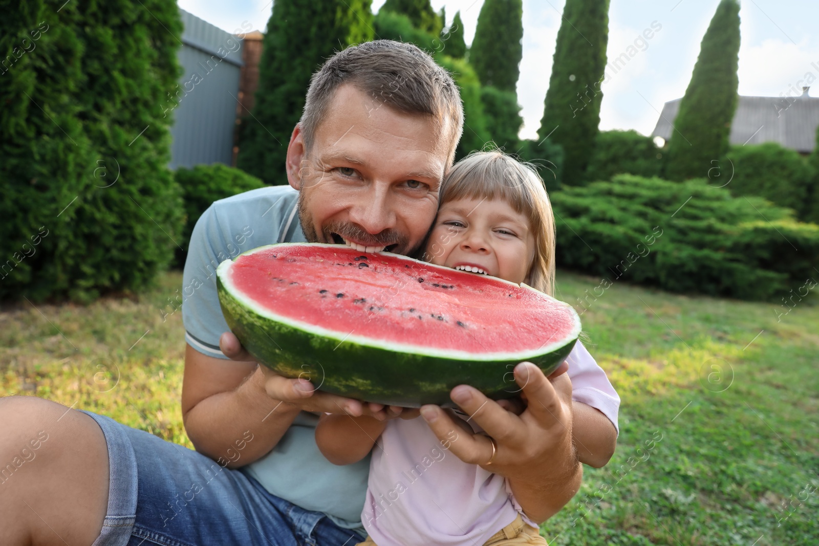 Photo of Man and his cute daughter eating juicy watermelon outdoors together