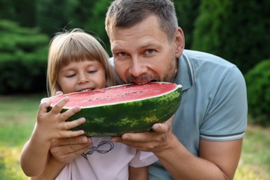 Photo of Man and his cute daughter eating juicy watermelon outdoors together