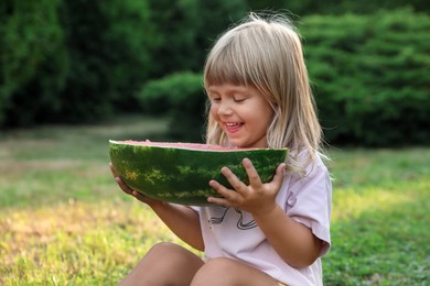 Cute little girl with half of juicy watermelon on green grass outdoors