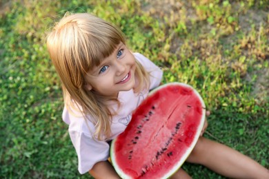 Photo of Cute little girl with half of juicy watermelon on green grass outdoors, above view