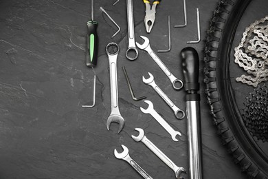 Parts of bicycle and tools on black table, flat lay. Space for text