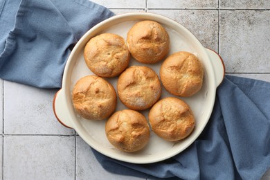 Photo of Baking dish with homemade tasty buns on textured tiled table, top view