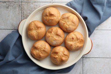 Photo of Baking dish with homemade tasty buns on textured tiled table, top view