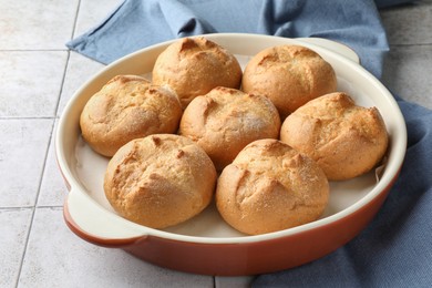 Photo of Baking dish with homemade tasty buns on textured tiled table, closeup