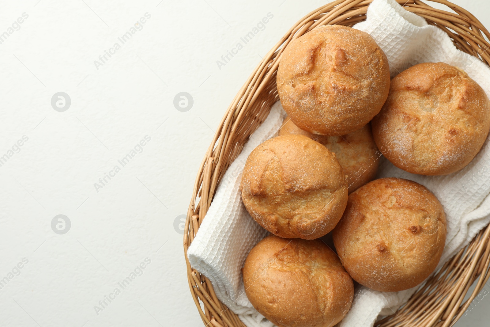 Photo of Wicker basket with homemade tasty buns on white table, top view. Space for text