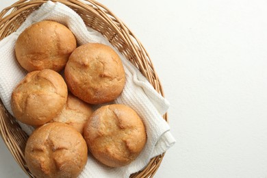 Wicker basket with homemade tasty buns on white table, top view. Space for text